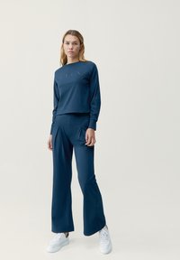 Mörkblå träningsset bestående av en långärmad topp med rund hals och avslappnad passform, tillsammans med löst sittande byxor och vita sneakers.