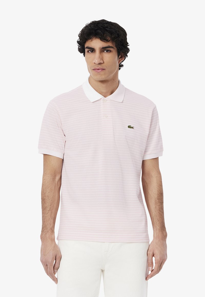 Polo shirt a righe rosa chiaro con maniche corte e colletto bianco. Presenta un logo verde Lacoste sul lato sinistro del petto. Tessuto morbido al tatto.