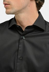 Svart skjorta med knappar i slät tyg, med klassisk krage och två knappar på knäppningen, sedd från nackområdet.