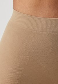Beige high-waisted leggings with a ribbed waistband and a textured fabric featuring subtle patterns and a soft, smooth surface.