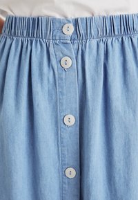 Gonna di jeans azzurro chiaro con vita arricciata e cinque grandi bottoni bianchi rotondi sul davanti. Texture liscia e design casual.