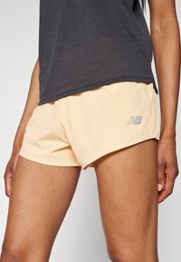 Heledad virsikavärvi, aukude ja elastse vöökoha ning hõbedase New Balance'i logoga lühikad püksid. Kangas näib olevat hingav ja sobib sportimiseks.