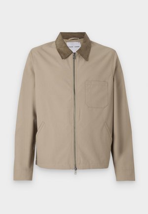 Beige jakke med en brun ruskinds krave, lynlås foran, to sidelommer og en brystlomme. Glat tekstur og moderne design.