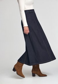 Dunkelblå denim A-linje kjol med kontrasterande gula sömmar, med hög midja, och bärs tillsammans med bruna mocka ankelstövlar.