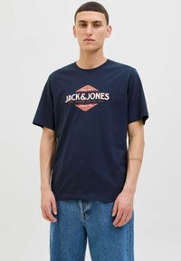 Tamsiai mėlyna medvilninė marškinėlių su apvaliu iškirpimu, ant priekinės dalies turi retro stiliaus Jack & Jones logotipą raudona ir balta spalvomis, laisvas kirpimas, trumpomis rankovėmis.