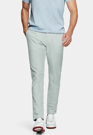Un pantalon rayé vert clair en tissu doux, avec une coupe slim et des poches latérales, associé à des baskets blanches.