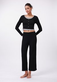 Black crop top with gray accents and button details, paired with loose black pants. Made from soft, stretchable fabric.
