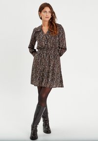 Black dress with multicolored floral print, elastic waist, long sleeves, and collar. Paired with knee-high black boots featuring studs.