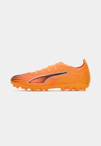 Botín de fútbol de un naranja brillante con parte superior texturizada, forma aerodinámica, acentos en negro y plata, y tacos moldeados para tracción.