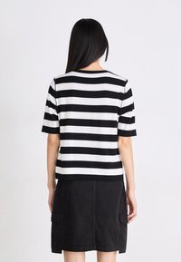 Zwart-wit gestreept T-shirt met korte mouwen en een ronde hals. Zachte stof. Gedragen met een zwarte rok met zijzakken.