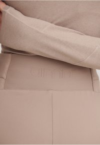 Lys beige treningsleggings har en teksturert midjebånd med preget merkevare. Mykt, glatt stoff med rene sømmer og et strømlinjeformet design.