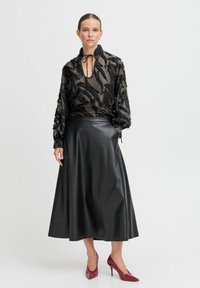 Blusa nera trasparente con motivi a foglia testurizzati, fiocco alla gola e maniche lunghe abbinata a una gonna nera in ecopelle fino al ginocchio e tacchi bordeaux.