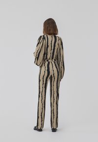 Beige and black striped jumpsuit with long, puffed sleeves, fitted waist, and wide-leg pants. Textured fabric with a dynamic pattern.
