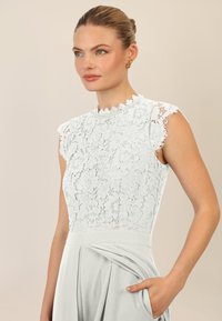 Top de encaje azul claro con mangas cortas y escote ondulado, combinado con una suave falda gris plisada. La tela tiene un delicado patrón floral.