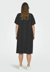 Rochie midi neagră cu mâneci scurte și buline albe. Are o croială lejeră și este confecționată dintr-un material moale. Este purtată cu adidași albi.