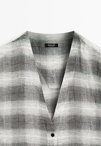 Kortarmige shirt, grijs en witte gestreepte patroon, lichtgewicht stof, V-hals, enkele zwarte knoopdetail, label zichtbaar bij de kraag.