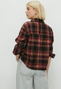 Red and black plaid flannel shirt with a collared neckline, button cuffs, and a curved hem. Made from soft, textured fabric.