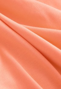 Tessuto di colore pesca con una texture liscia, che mostra pieghe e grinze, realizzato in materiale leggero ed elastico.