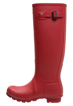 Red rubber rain boot with a high shaft, rounded toe, textured sole, and a metallic buckle accent on the side. Smooth surface and flexible design.