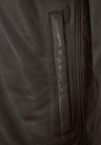 Braune Lederjacke mit glatter Textur und einer Seiten Tasche mit rechteckigem Deckel. Nähte sind entlang der Kanten sichtbar.