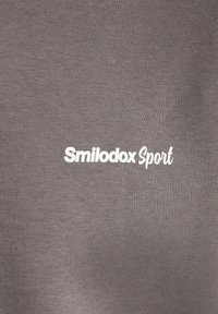 Camiseta deportiva gris con una textura suave, similar al algodón, que presenta el lema "Smilodox Sport" en letras blancas en el frente.