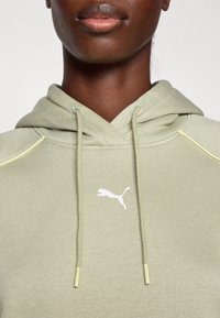 Sweatshirt verde-claro com acabamentos texturizados, apresentando um logotipo branco da Puma no peito e detalhes amarelos nas costuras dos ombros.