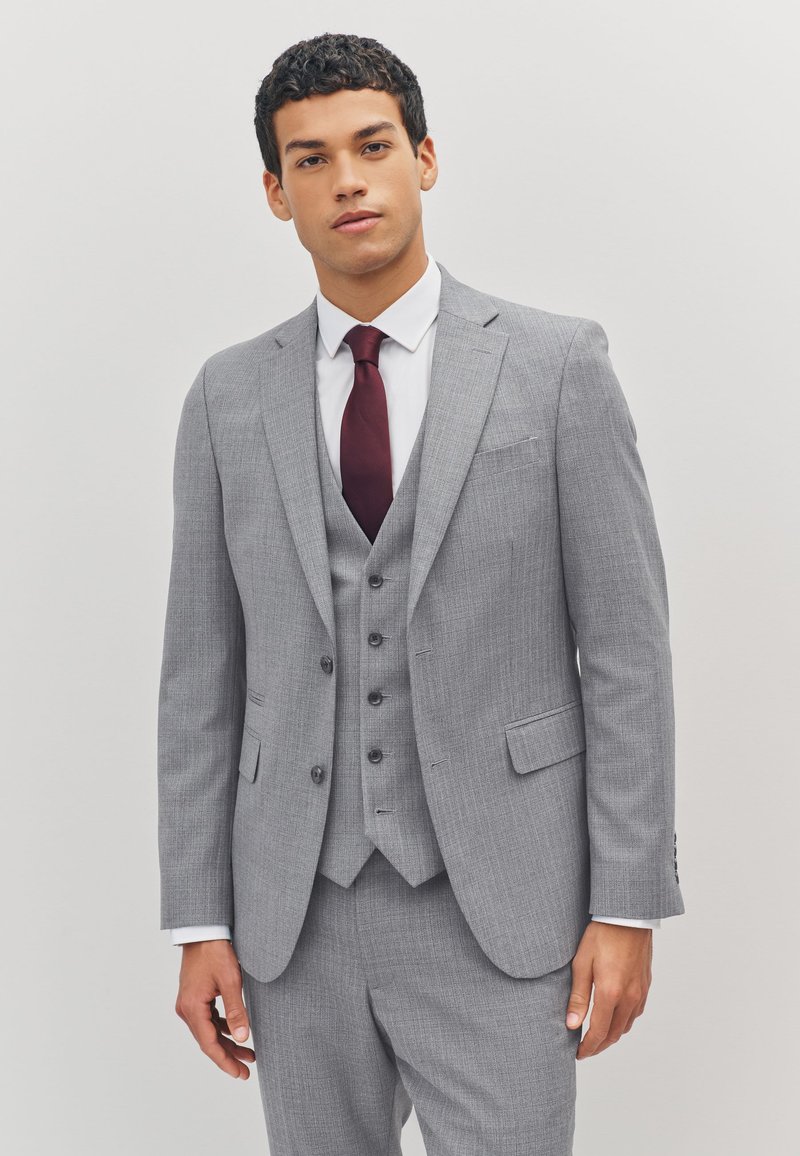 Costume trois pièces gris clair avec une finition texturée, des revers crantés et une cravate bordeaux. Comprend des boutons sur le gilet et le pantalon.