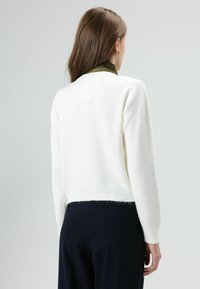 Pull blanc tricoté à coupe courte, ourlet côtelé et manches longues. Texture douce et moelleuse, avec un dos sans coutures.