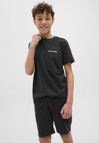 Crna pamučna majica s okruglim izrezom i kratkim hlačama; na majici se nalazi bijeli logo "JACK & JONES". Jednostavan, ležeran dizajn.