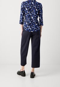 Top azul marino con patrón de formas abstractas; mangas de tres cuartos. Combinado con pantalones de pierna ancha en un azul marino oscuro y zapatos de plataforma negros.