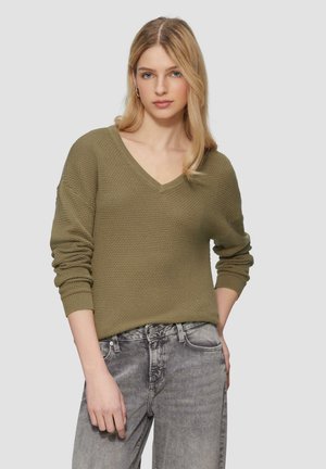 Pull en maille vert olive avec un col en V, coupe décontractée et manches à côtes, associé à un jean gris clair.