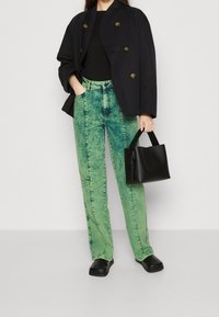 Groene acid-wash denim broek met een recht model, gecombineerd met een zwarte oversized dubbelgeknoopte blazer en een kleine zwarte handtas.