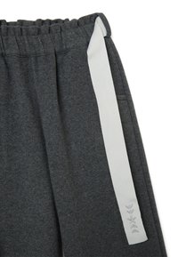 Pantalons de survêtement gris avec une taille élastique, présentant une bande blanche sur le côté et des accents brodés sur la bande. Tissu doux et texturé.