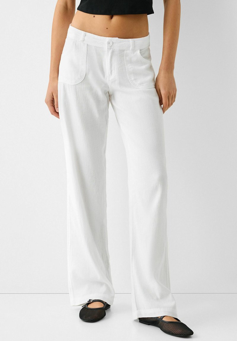 Hvide brede benbukser lavet af bomuld med høj talje, to forlommer og en tekstureret overflade. Sammen med sorte mesh-sko.