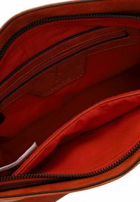 Interior de bolso de cuero en un rojo vibrante con una textura suave, cuenta con un bolsillo con cremallera, un bolsillo adicional tipo deslizante y detalles en cremallera negra.