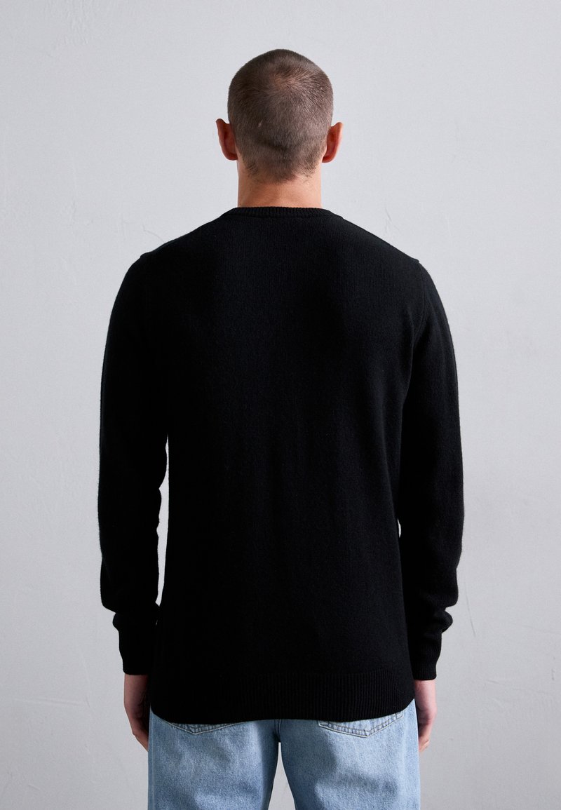 Schwarzer Pullover mit langen Ärmeln und Rundhalsausschnitt; aus weichem Material gefertigt, mit geripptem Saum und Bündchen; getragen mit hellblauen Jeans.