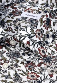 Chemise blanche à boutons avec un motif floral dense rouge, vert et noir, et étiquette "seidensticker" à l'intérieur du col.