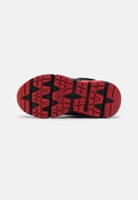 Suela de zapatilla atlética negra con una suela de goma negra y roja texturizada, que presenta un patrón de tacos distintivo para ofrecer tracción.