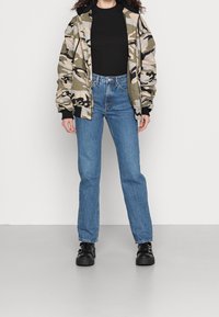 Chaqueta de camuflaje con un corte relajado, combinada con unos vaqueros azules de cintura alta. Botas de plataforma negras con detalles de hebilla completan el conjunto.