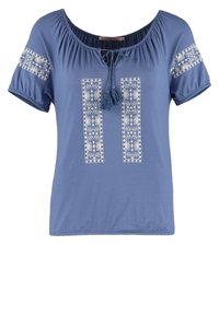 Haut bleu à manches courtes avec broderies florales blanches, deux panneaux verticaux centraux et un col à cordon de serrage avec un détail à pompon.