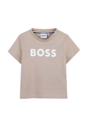 Camiseta beige de manga corta para niño pequeño con texto "BOSS" en blanco en el frente y dos pequeños botones a presión en el hombro izquierdo.