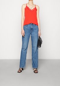 Camiseta roja con encaje, combinada con jeans de cintura alta azules, sandalias negras con tiras y un pequeño bolso negro.
