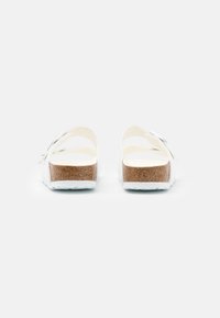 Witte sandalen met een open achterkant, kurken voetbed en twee gebogen banden. Textuurzool met ribbels voor grip, met een eenvoudig ontwerp.