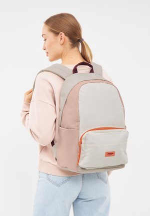 Zaino in grigio chiaro e rosa pallido, con una tasca frontale con zip arancione. Tessuto liscio, spallacci imbottiti e maniglia superiore.