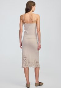 Beige gebreide tanktop met spaghettibandjes, gecombineerd met een knielange rok met bloemenkant aan de onderrand. Getextureerde gebreide stof.