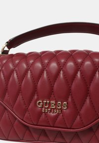 Rode gewatteerde handtas van leer met een gouden logo "GUESS EST1981" en een korte handgreep. Geproduceerd oppervlak met diamantpatroon details.