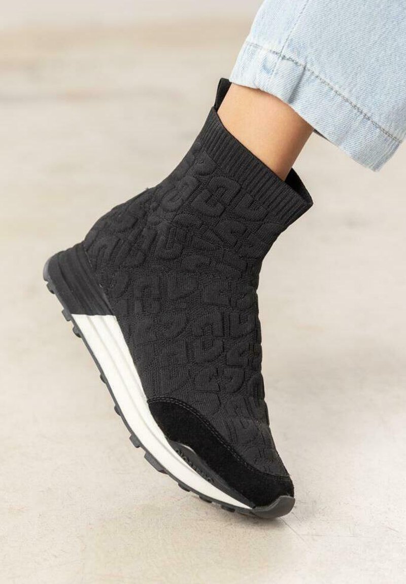 Botte chevillère tricotée noire avec motif texturé, dotée d'une semelle intermédiaire blanche et d'une semelle extérieure en caoutchouc noir. Le design inclut un col élastique pour un ajustement confortable.