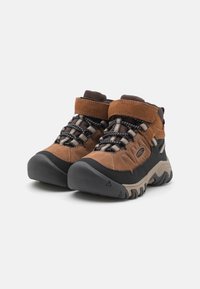 Braune Wanderschuhe mit einem oberen Material aus Wildleder und Synthetik. Ausgestattet mit einer strukturierten Gummisohle in Schwarz, Schnürung und einem gepolsterten Schaft für zusätzlichen Komfort.