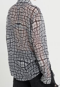 Chemise transparente à carreaux en noir, blanc et marron ; dotée d'un col classique et de manches longues avec poignets à boutons, ourlet légèrement arrondi.