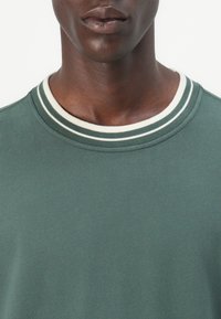 Green sweatshirt featuring a crew neckline with white and dark green striped accents. Soft texture, medium weight fabric, and a simple design.